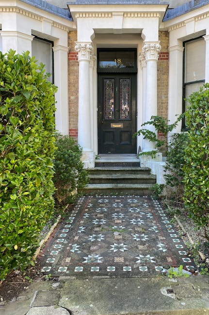 This image shows the entrance to a traditional Victorian-style townhouse, featuring a black front door with decorative stained glass panels and a brass mail slot, set within a white stucco façade acc